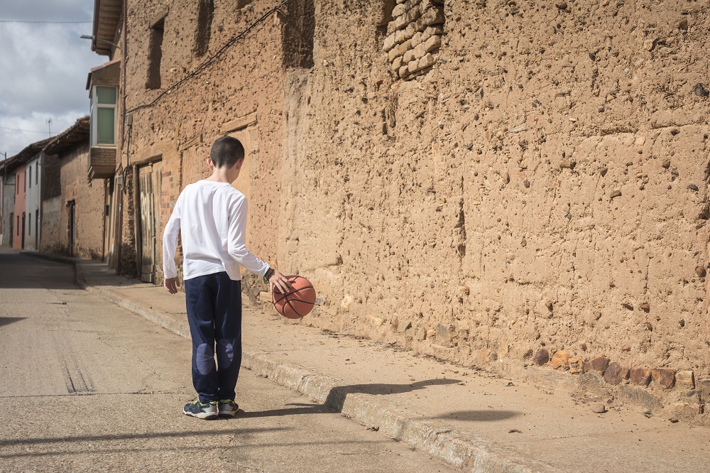 Un niño jugando con una pelota en una calle vacía.