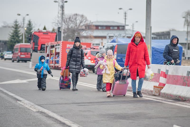 Familias ucranianas salen por la frontera de su país portando maletas.